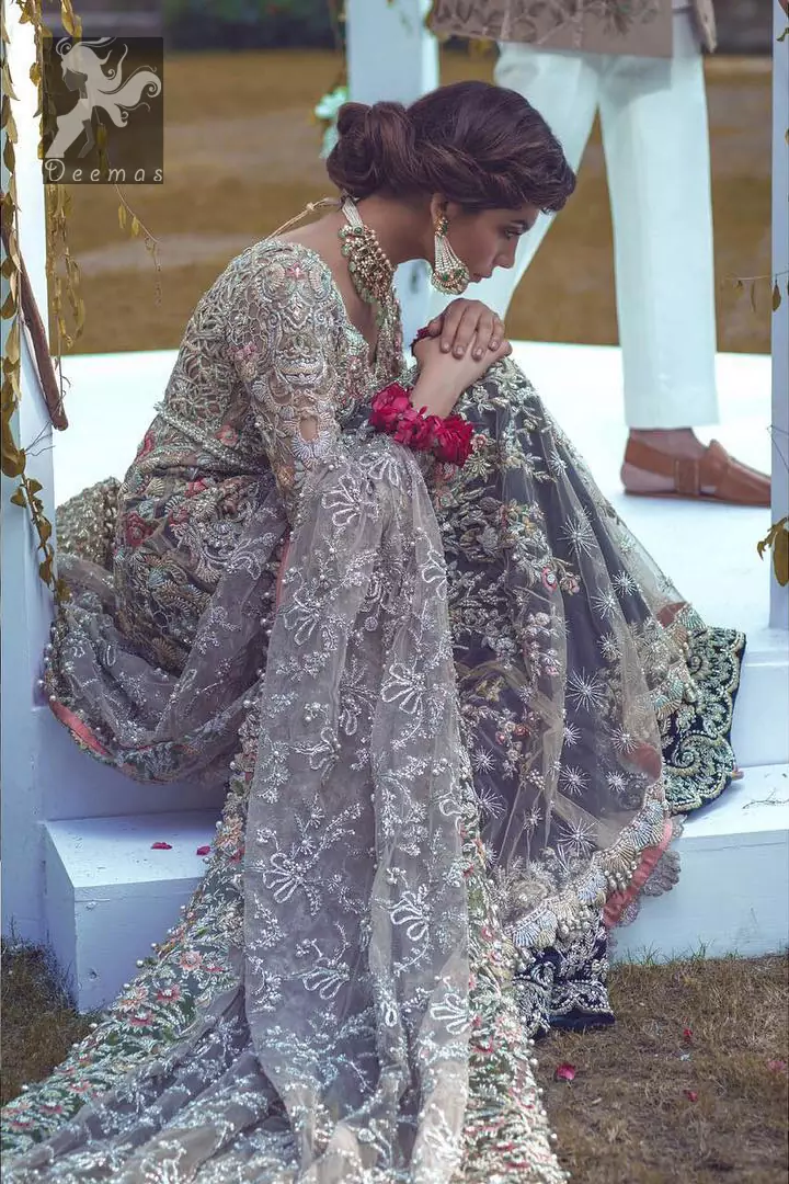 Light grayish fawn net maxi and dupatta. Bridal maxi adorned with silver, light golden, antique shades and colorful thread embellishment. Light grayish fawn net dupatta adorned with embellished border and large motifs all over it. Blackcurrant velvet sharara adorned with silver and light golden embellished border.