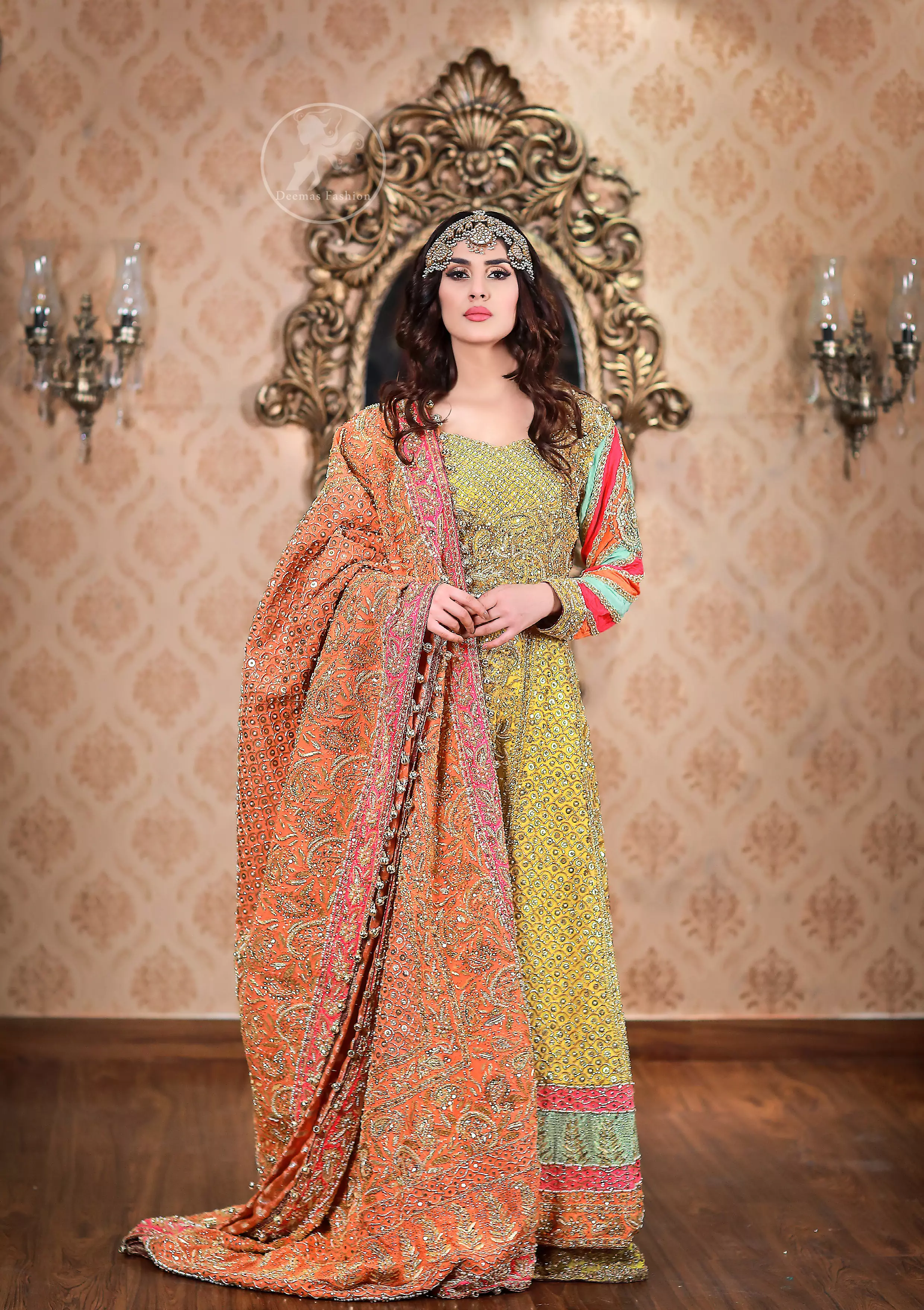 This outfit is decorated with antique shaded embroidery. The dress is fully embellished. Sleeves are decorated with different colour applique which adds to the look. It is adorned with thick embellished appliqued borders. It comes with yellow sharara and sequins spray all over it . It is coordinated with orange raw silk heavy embellished dupatta which has embellished with pink appliqued borders and beautiful tassels.