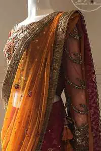 This dress is beautifully sculptured with floral embroidery. It is adorned with intricate detailing embellishment with antique gold kora dabka, tilla, kundan and swarovski. The blouse has full length sleeves decorated with floral motifs. It is coordinated with hot pink banarsi lenhengha finished with golden gota lace at the bottom. It is enhanced with floral motifs. The outfit is beautifully coordinated with orange pallu style dupatta embellished with golden Gotta lace on all sides.