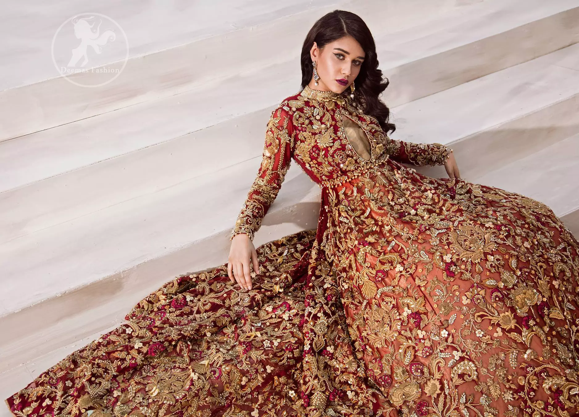 The grand maroon bridal stands out due to its uniqueness and the perfect fusion of modern cut and traditional embroidery. This halter neckline maxi is done with heavy embellishment of golden kora dabka, kundan, tilla, pearls and sequins work. It is further ornamented with detailed floral motifs. It is coordinated with brocade churidar pajama.