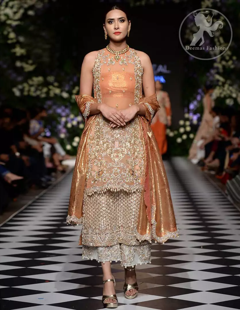 This outfit is stunningly perfect for any evening ensemble. It is paired with a sleeveless double layered shirt in organza fabric which is extensively hand worked in crystals and zardozi. This dress is beautifully sculptured with dull golden floral embroidery, adorned with cutwork borders embellished with tassels, kora, dabka, pearl and sequins work all over. It comes with embroidered trousers. It is coordinated with tissue dupatta which is furnished with four sided scalloped border.