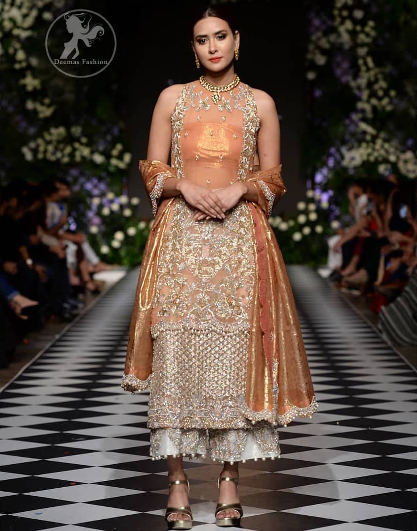This outfit is stunningly perfect for any evening ensemble. It is paired with a sleeveless double layered shirt in organza fabric which is extensively hand worked in crystals and zardozi. This dress is beautifully sculptured with dull golden floral embroidery, adorned with cutwork borders embellished with tassels, kora, dabka, pearl and sequins work all over. It comes with embroidered trousers. It is coordinated with tissue dupatta which is furnished with four sided scalloped border.