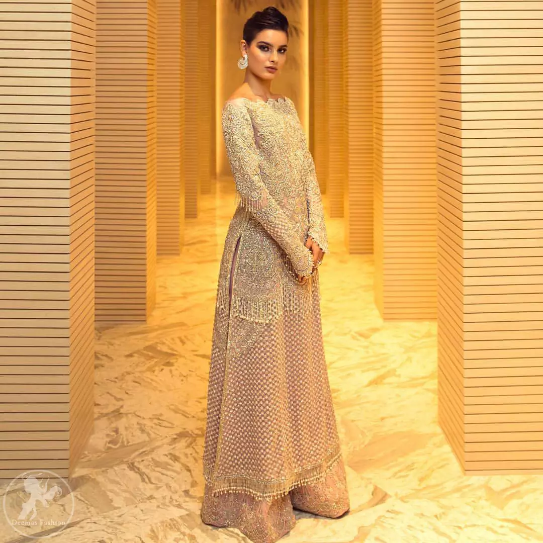 Boost your confidence and style in this glamorous attire accentuated with finest thread and zardosi work embroidery. This outfit paired up with salmon pink off shoulder long shirt embellished with thread embroidery and dull golden kora, dabka, sequins and tassels. It comes with beautifull sharara enhanced with floral motifs on the bottom. It is coordinated with chiffon dupatta which is sprinkled with sequins all over it.
