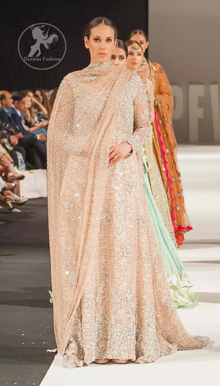 The bridal stands out due to its uniqueness and the perfect fusion of modern cut and traditional embroidery. This dress is beautifully decorated with heavy embroidery. It is highlighted with kora, dabka, tilla, sequins and pearls. It comes with embroidered sharara. It is coordinated with tissue dupatta which is sprinkled with sequins all over it. It is further furnished with four sided scalloped border.
