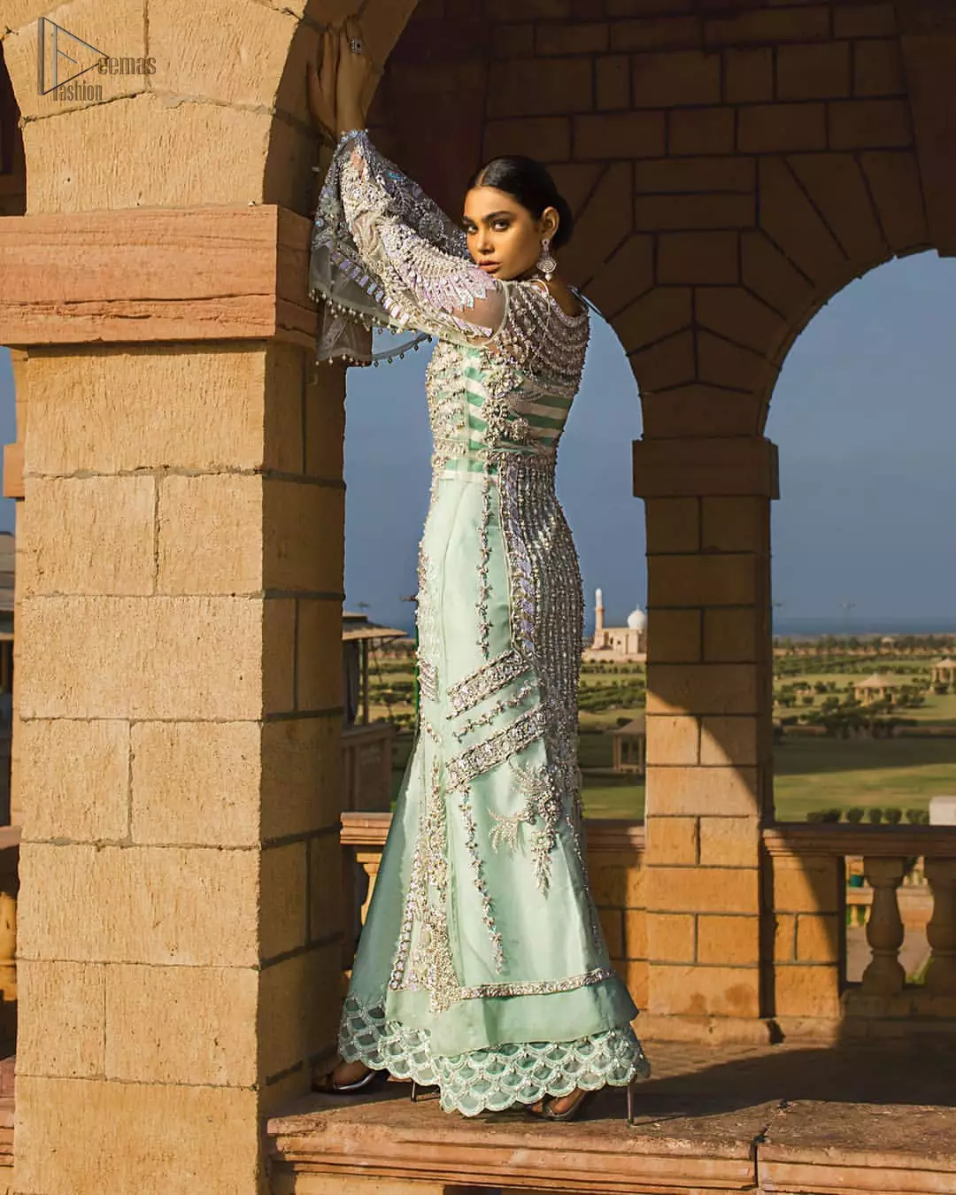 Take a step towards refreshing your wardrobe with aqua front open gown and palazzo pants. This front open gown is perfected with loaded light golden and silver work. The front of the gown is heavily embellished with different styles motifs and rich embellishment on bodice. Furthermore the back of the gown and bell sleeves are also decorated with detailed embroidery and dangling balls. The palazzo pants with it is made of raw silk fabric with lace detail on the bottom. The outfit is coordinated with aqua organza dupatta sprinkled with sequins all over.