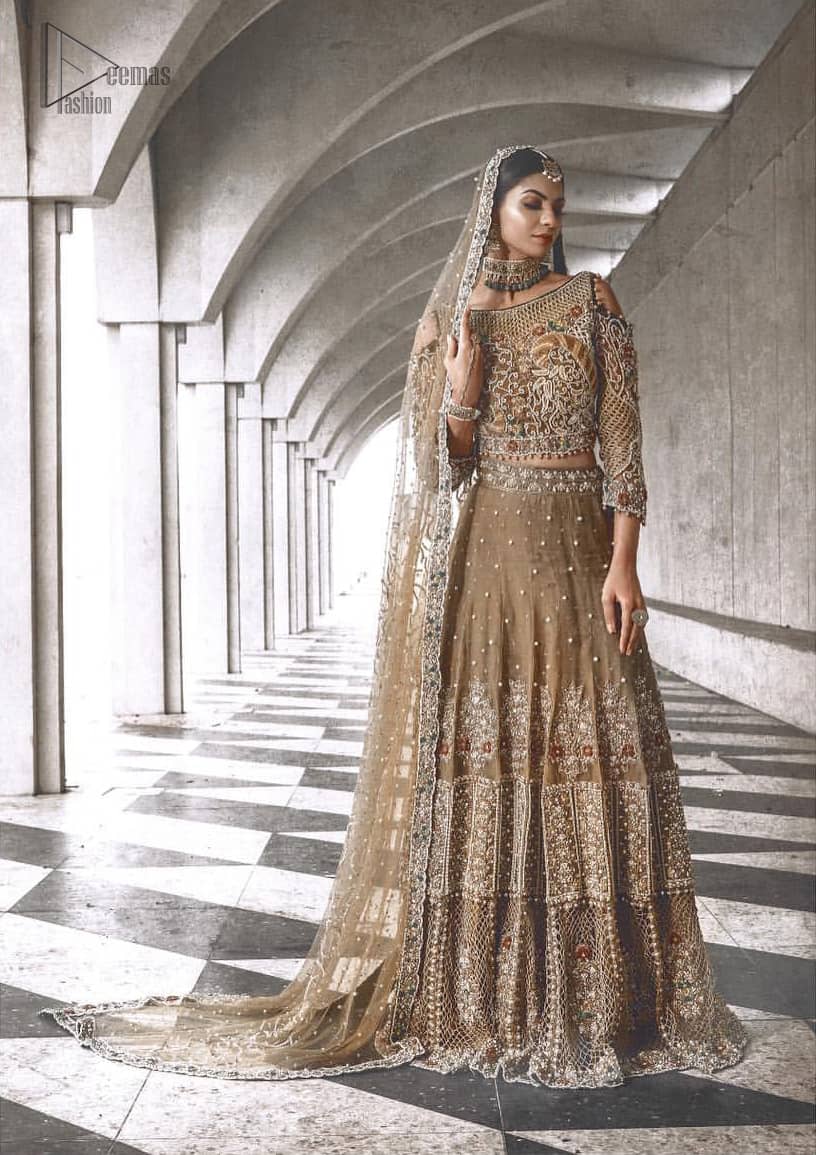 An example of beauty and elegance. Our bride makes a statement in this stunningly floraison, perfect blend of glamour and tradition with outstanding craftsmanship and gorgeous detailing. The cold shoulder blouse is stunningly embellished with intricate embroidered neckline done with light golden and silver zardosi work all over. Lehnga is compiled with zardozi embellishment which gives this festive season a flattering dimension to die for. The outfit is coordinated with beige net dupatta adorned with scattered sequins all over and four sided border.