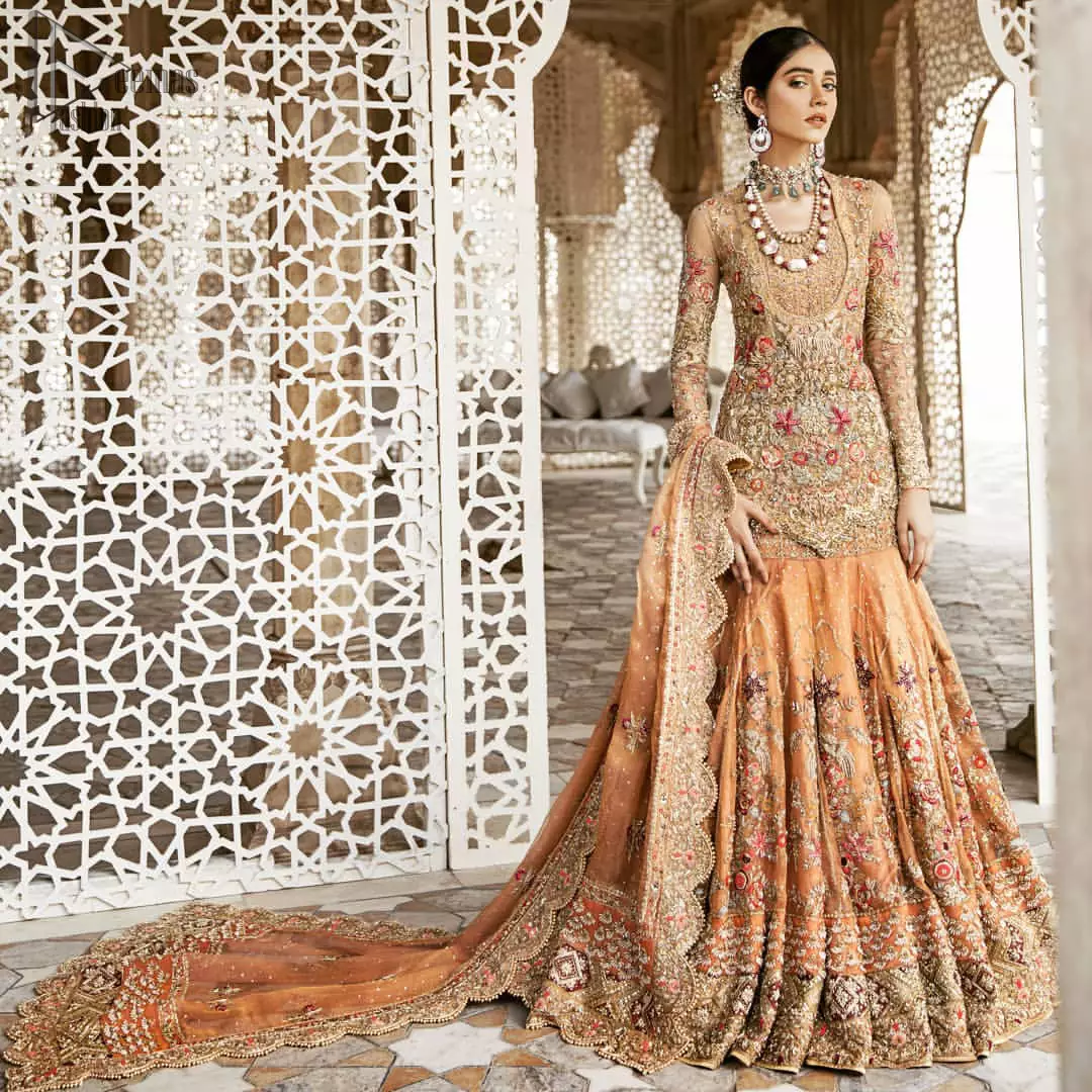 Beautifully elegant with a modern twist. Adorned in an orange embellished with antique detailing all over, this undeniably elegant attire will elevate your style. The shirt is ornamented with antique zardozi and multiple color embroidery detailing all over and vibrant floral motifs. Furthermore the hemline of the shirt is in cutwork style which adds twist. Paired it up with heavily embellished lehenga. The dupatta incorporates beautifully designed scalloped borders on all four sides, focusing on the heavily embellished pallu borders to give it a perfect look.
