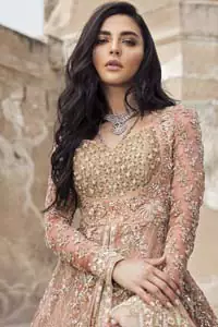 This garnet ensemble is sure to make you look like glamorous royalty with immaculate work covering every inch of the frock. The bodice of the frock is heavily embroidered with champagne zardozi work. Furthermore the hemline is ornamented with geometric patterns. It is coordinated with peach and light pink lehenga with a flowing train embellished with light golden and champagne embroidery and scattered floral motifs in a sequence.  this is an ensemble that deserves to be flaunted. Style it up with light pink dupatta having four sided embroidered border.