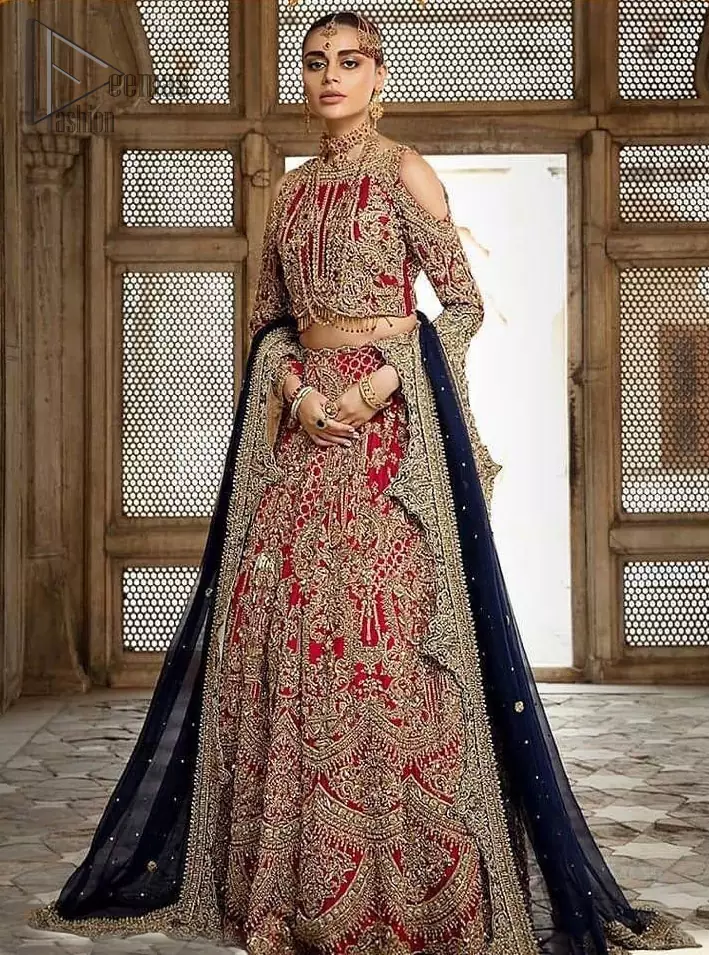 A breathtaking red traditional lehenga  paired with a detailed blouse, equally alluring make for an ensemble which is comfortably chic. The blouse is done with golden and antique shaded embroidery and finishing with tassels. Blouse having cold shoulder full sleeves. The lehenga is enhancing with the art of classical heritage showcasing the craftsmanship of kora, dabka, tilla, kundan and sequins detailed, artistically embellished to give a beautiful rhythm to the outfit. It comprises with navy blue dupatta sprinkled with sequins and four sided scalloped border. This is an ensemble that is sure to invite compliments galore.
