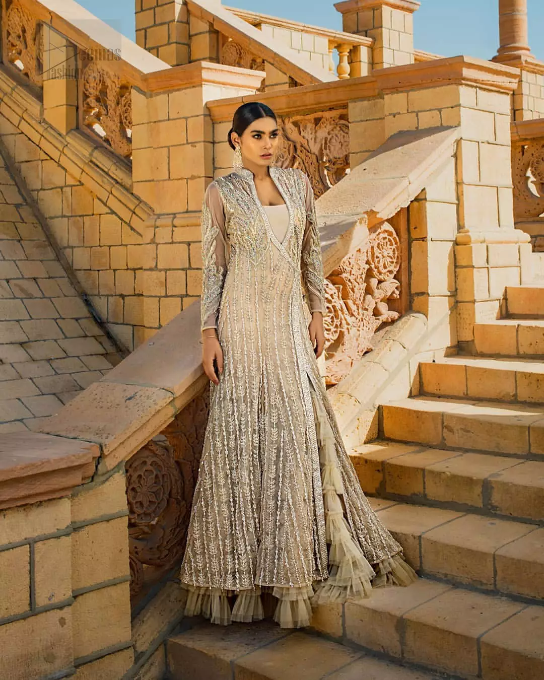 A fusion of traditional and latest fashion making the outfit trendy and unique. This angrakha style floor length maxi is heavily hand crafted with floral embroidery on the bodice, floral booties and vertical lines all over the dress. Back is also enhanced with vertically designed floral booties and swarovski crystals lines all over. The embroidery is done in the shades of silver and dull golden zardozi work. Style it up with frilled lehenga to give it a regal look. This outfit is comprises with fawn net lehenga sprinkled with sequins spray all over.