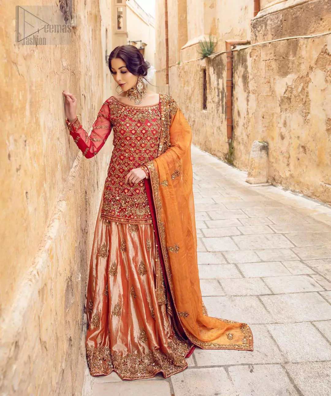 Make your big day more beautiful with our excessively embroidered back train lehenga shirt featuring delicately embellished neckline along with geometric patterns highlighted in antique shaded embroidery detailing and intricately embroidered borders that gives perfect ending to this outfit. Pair it up with a breathtaking back train lehenga with scattered motifs on the ground and embellished hemline. The orange organza dupatta with floral motifs and finishing all around the edges makes the look complete. The combination of orange with red is absolutely breathetaking.