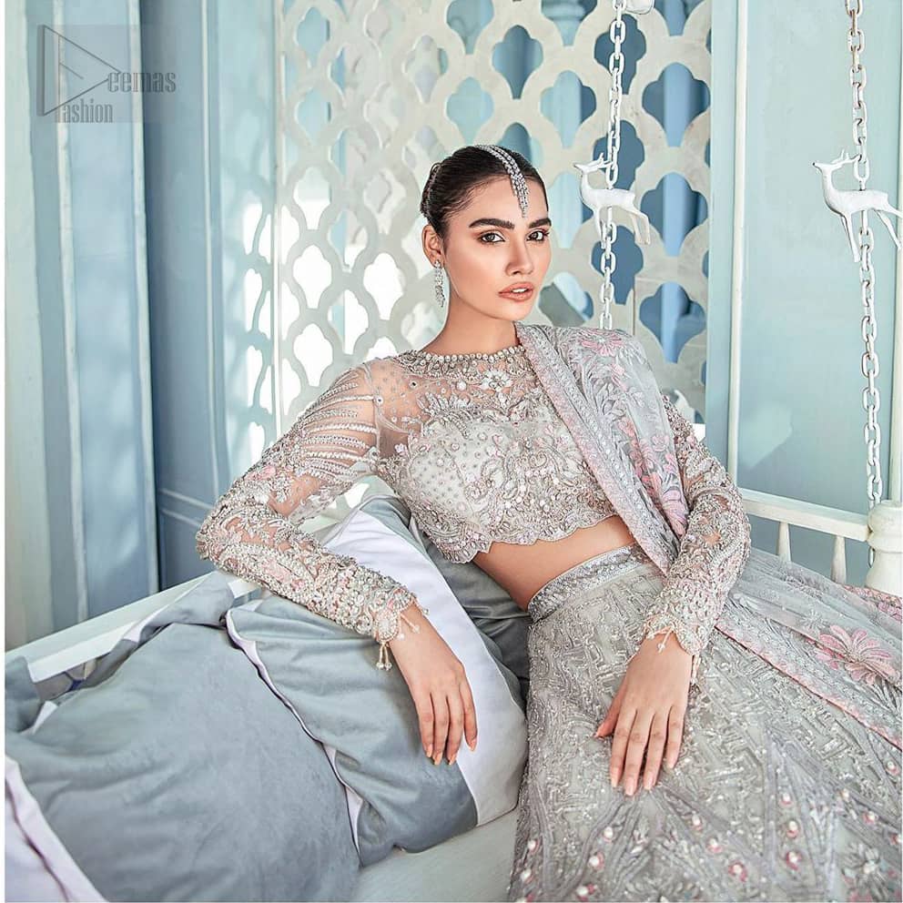 Its an unforgettable look that will effortlessly take you from day to night this festive season. Unique craftsmanship and detailed embellishments bring heavenly hued gossamer fabrics to life, creating delicate yet flamboyant pieces of art in our collection. The light gray blouse is delicately crafted with silver zardozi embellishment and finishing with scalloped sleeves and tassels. It is coordinated with lehenga which is heavily laden with sumptuous details of zardozi, applique, kora and dabka. Furthermore the lehenga is enhansed with pink applique bottom. Complete the look with light gray organza dupatta with rich embroidered floral motifs places artistically on the dupattas pallu gives a royal look.