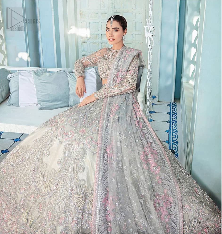 Its an unforgettable look that will effortlessly take you from day to night this festive season. Unique craftsmanship and detailed embellishments bring heavenly hued gossamer fabrics to life, creating delicate yet flamboyant pieces of art in our collection. The light gray blouse is delicately crafted with silver zardozi embellishment and finishing with scalloped sleeves and tassels. It is coordinated with lehenga which is heavily laden with sumptuous details of zardozi, applique, kora and dabka. Furthermore the lehenga is enhansed with pink applique bottom. Complete the look with light gray organza dupatta with rich embroidered floral motifs places artistically on the dupattas pallu gives a royal look.