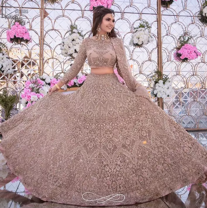 Picturing your bridal in a tea rose colour? This subtleness laden with ornamental embellishments and embroidery creates such a fairytale touch to your wedding. The boat-shaped blouse is emphasized with light golden zardozi work and finished with dangling pearls. Paired up with matching lehenga creates an unusual charisma wholeheartedly. Featuring beautiful handwork and a delicate arrangement of hand-embellished floral patterns with zardozi work along the length of lehenga. Refined craftsmanship is at its best with a hand embellished dupatta. The dupatta incorporates beautifully designed borders on all four sides, focusing on the heavily embellished pallu borders to give it a perfect maharani look.