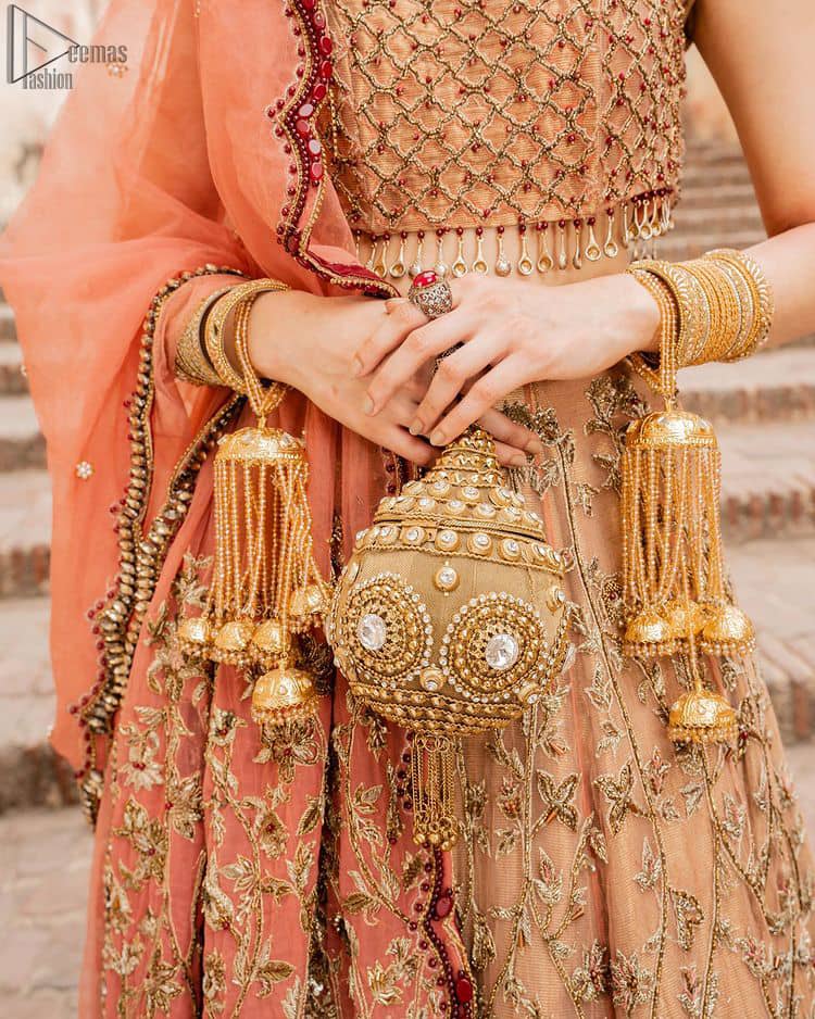 Crafted with love. This beautiful bride is a vision of impeccable grace and elegance in a divinely crafted bridal couture, with the exquisite embroideries that add the royal touch to the outfit. This off-shoulder blouse is meticulously crafted with zardozi work in the shades of golden and antique, finished the blouse with dangling tassels. The lehenga is emphasized with hand embellished floral embroidery with kora, dabka, tilla, sequins and beads all over. The look is complete when it gets paired up with an organza dupatta having scalloped finishing along the length and floral jaal on both sides of pallu.