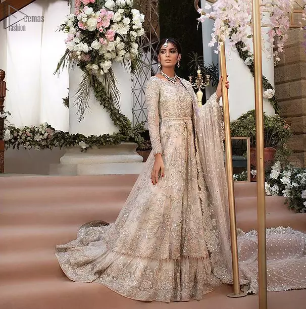 Beautiful Pakistani wedding dress in light peach front open pishwas with back train lehenga and emrboidered dupatta. This outfit brings drama and playfulness to traditional front open pishwas and lehenga with a modern approach. The mix of colours embroidery much of a choice for the festive season. The neckline is artistically decorated with kora, dabka, tilla, sequins and thread work. The rest of the outfit is adorned with floral bootis and finished with a scalloped hemline. Complete the look with an artfully coordinated lehenga which is ornamented with a bold and captivating back trail design with a traditional intricate embroidered. The classically balanced borders on the pure organza dupatta add exquisiteness to the look.