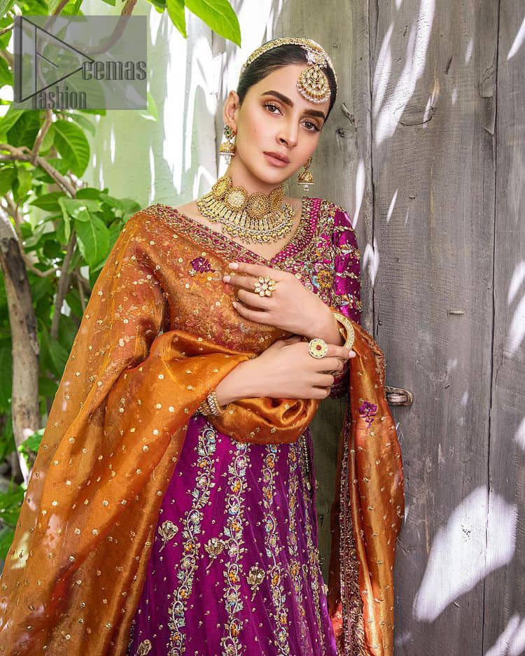 The outfit defines the true essence of allure with its spellbinding magenta hue and intricate details. The blouse is decorated with golden embroidery based on the neckline and sleeves. The sleeves are further enhanced with the embellished handwork. It is Beautifully organized with a magenta lehenga that is again heavily embellished with golden embroidery that is just adding poise to the whole look. Paired along with an orange dupatta decorated with subtly adorned motifs and embellished border that is completing this Mehandi looks wondrously.