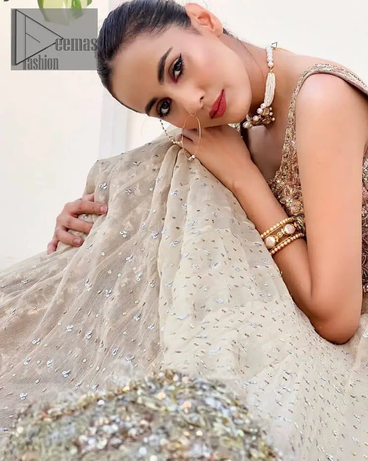 The perfect outfit for walima to enhance your glow. Starting this article with a dream rust blouse having a strap neckline and prominent sleeveless style to embrace the romantic culture. The following blouse is fully embellished with golden embroidery that is prominent with tilla, dabka, kora, pearls and sequins spray to fulfil your dreamy look. It is coordinated with an ivory can-can lehenga whose border is again rendered with golden embroidery and sequins sprayed all over to continue the look. Complete this outfit with a rust dupatta which is embellished with four-sided borders and sequins sprayed all over to enhance the glow of the bride.