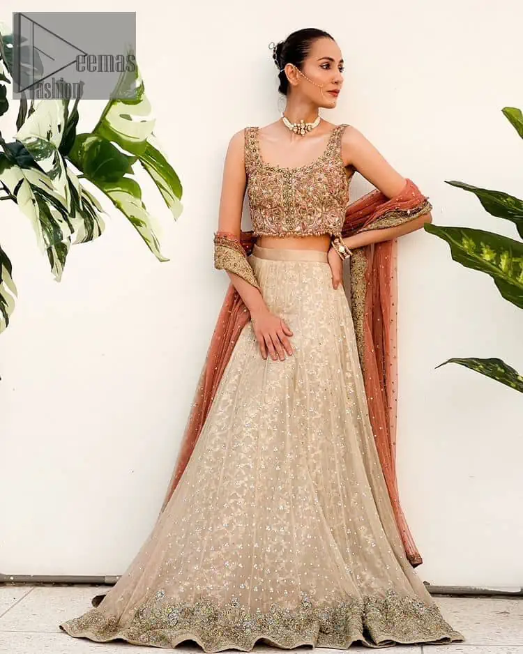 The perfect outfit for walima to enhance your glow. Starting this article with a dream rust blouse having a strap neckline and prominent sleeveless style to embrace the romantic culture. The following blouse is fully embellished with golden embroidery that is prominent with tilla, dabka, kora, pearls and sequins spray to fulfil your dreamy look. It is coordinated with an ivory can-can lehenga whose border is again rendered with golden embroidery and sequins sprayed all over to continue the look. Complete this outfit with a rust dupatta which is embellished with four-sided borders and sequins sprayed all over to enhance the glow of the bride.