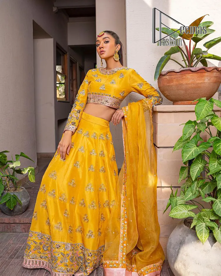 Yellow is just associated with mehndi as the sun is associated with brightness. DeemsFashion presents the bright yellow Pakistani mehndi outfit which laboriously begins with a blouse which is handsomely hand-rendered with silver and copper embroidery to make your day super duper bright. The boat shape neckline and full sleeves of this Pakistani mehndi outfit add to the breathtaking dream of the bride. It is paired up with a lehenga in the same colours which is adorned with floral motifs and bordered embroidery as well. Complete this Pakistani mehndi outfit with a dupatta in the same colour which is adorned with a four-sided embellished border and sequins sprayed all over.