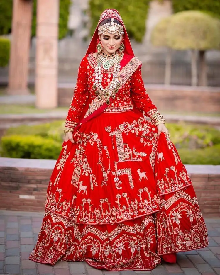 Take off that shyness and wear some deep red reception dress. DeemasFashion presents a very unique reception dress in deep red colour which is starting from a deep red blouse style up with a boat shape neckline and full sleeves to give you a romantic look. Further, it is prominent with golden embroidery which involves tilla, dabka, kora and crystal all over. It is systemized with a double-layer lehenga having lovely heavy embroidery to increase your handsome number. Complete this reception wear with a dupatta which is sprinkled with sequins all over it. It is further furnished with a four-sided scalloped border.