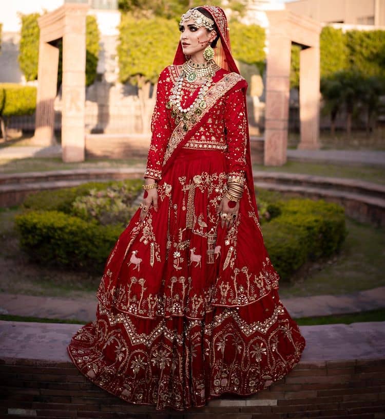 Take off that shyness and wear some deep red reception dress. DeemasFashion presents a very unique reception dress in deep red colour which is starting from a deep red blouse style up with a boat shape neckline and full sleeves to give you a romantic look. Further, it is prominent with golden embroidery which involves tilla, dabka, kora and crystal all over. It is systemized with a double-layer lehenga having lovely heavy embroidery to increase your handsome number. Complete this reception wear with a dupatta which is sprinkled with sequins all over it. It is further furnished with a four-sided scalloped border.