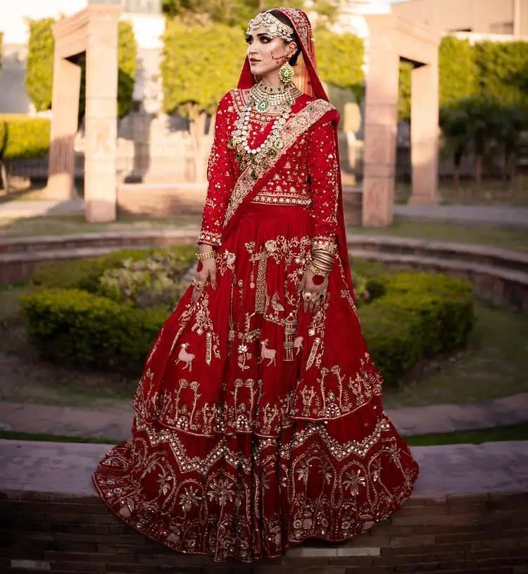 Take off that shyness and wear some deep red reception dress. DeemasFashion presents a very unique reception dress in deep red colour which is starting from a deep red blouse style up with a boat shape neckline and full sleeves to give you a romantic look. Further, it is prominent with golden embroidery which involves tilla, dabka, kora and crystal all over. It is systemized with a double-layer lehenga having lovely heavy embroidery to increase your handsome number. Complete this reception wear with a dupatta which is sprinkled with sequins all over it. It is further furnished with a four-sided scalloped border.