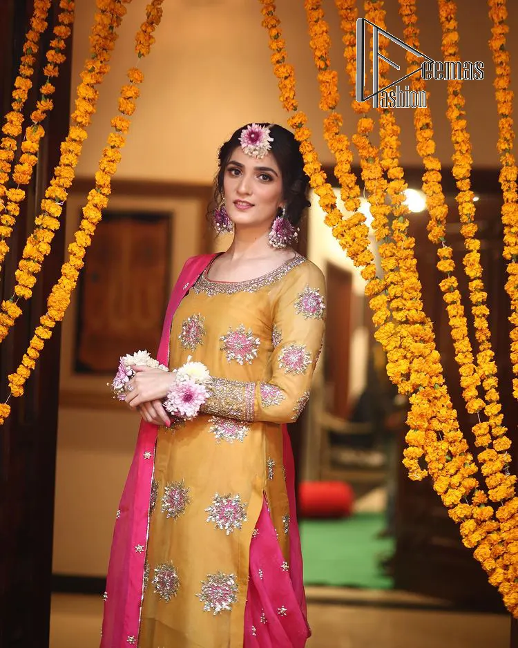 We seek outside the wonders we carry inside us. A mehndi dress in the mustard shirt is enhanced with gorgeous gota work. and is designed using the floral technique in pink and golden which is incrusted with tilla, dabka, kora and Sitara. The border of the mustard shirt is heavily ornamented with golden embroidery. The round neckline enhances the beauty of this mehndi dress when comes with three-quarter sleeves. It is paired up with mustard Gharara which is super simple and its border is encapsulated with Kiran. Complete this mehndi dress with a pink dupatta having ting floral motifs all over.
