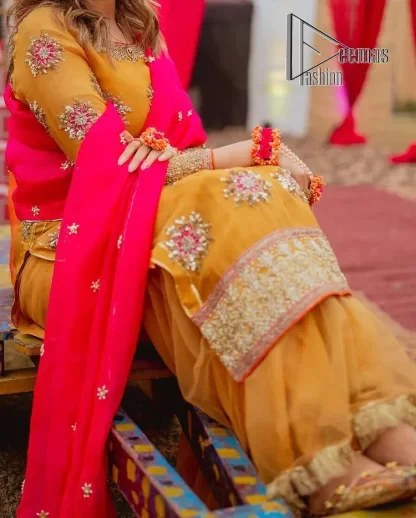 We seek outside the wonders we carry inside us. A mehndi dress in the mustard shirt is enhanced with gorgeous gota work. and is designed using the floral technique in pink and golden which is incrusted with tilla, dabka, kora and Sitara. The border of the mustard shirt is heavily ornamented with golden embroidery. The round neckline enhances the beauty of this mehndi dress when comes with three-quarter sleeves. It is paired up with mustard Gharara which is super simple and its border is encapsulated with Kiran. Complete this mehndi dress with a pink dupatta having ting floral motifs all over.