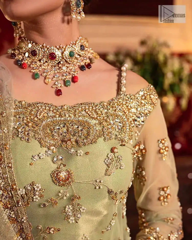 A refreshing colour palette that will make your eyes twinkle and heart sing! A pure organza short shirt in olive green is attractively hand-rendered with golden embroidery and is enhanced with naqshi, Sitara, dabka, tilla, and Zardozi. The strap neckline of this amazing shirt comes with full sleeves to make your Mehndi event more delightful and stunning. The following shirt is paired with double layered lehenga which is just in plane mode to balance the outfit. Complete this traditional look with a dupatta with sequins sprayed all over, framed with a gorgeous embellished four-sided border.