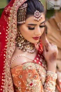 Shine bright in the sparkling ensemble from DeemasFashion. Introducing this reception outfit which begins with a rust pishwas.  This front en pishwas dipped in the richest shade of rust and is ornamented with golden embroidery which is further intensified with tilla, dabka, sequins and the real magic of zardozi. The strap neckline of the pishwas gives a unique aesthetic sense when comes with full sleeves. It is coordinated with an ivory lehenga whose border is embellished with golden embroidery. Finish this article with a dupatta framed with a four-sided embroidered border and sequin sprayed all over.