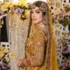 Take your style quotient up a few notches in this exquisite mehndi outfit! ]The maxi in mustard colour is a ravishing bridal attire with a magnificent elite and classy appearance. Gorgeous and glamorous multiple-colour embroideries enhance the showiness of this maxi.  It is further intensified with tilla, dabka, kora, Kundan and details of thread embroidery. Full sleeves, boat shape neckline and sparkling work make it a perfect traditional wear. It is coordinated with a scalloped dupatta in the same colour which is embellished with four-sided borders and floral motifs all over to make this outfit unique and aesthetic.