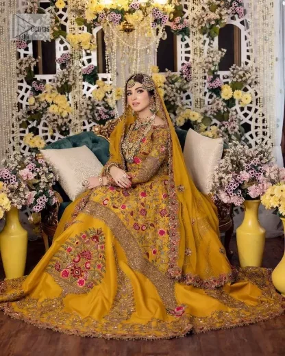 Take your style quotient up a few notches in this exquisite mehndi outfit! ]The maxi in mustard colour is a ravishing bridal attire with a magnificent elite and classy appearance. Gorgeous and glamorous multiple-colour embroideries enhance the showiness of this maxi.  It is further intensified with tilla, dabka, kora, Kundan and details of thread embroidery. Full sleeves, boat shape neckline and sparkling work make it a perfect traditional wear. It is coordinated with a scalloped dupatta in the same colour which is embellished with four-sided borders and floral motifs all over to make this outfit unique and aesthetic.