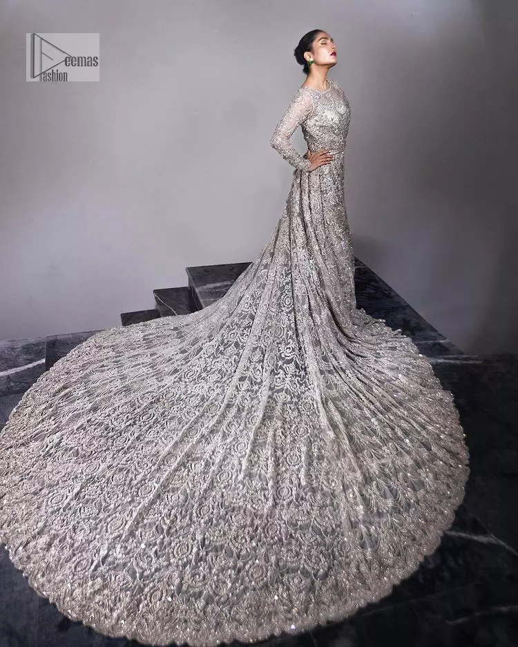 The trend of the back trains is still going strong as nikah wear – Here is the perfect one! This beautiful silver maxi is heavily embellished with silver embroidery. The gorgeous work of pearls, dabka, kora, Kundan and silver stones enhance the overall glamour of this maxi. The extraordinary design of the jewel neckline is completely embellished with silver stones and pearls embroidery combinations. The silver stones touch-up increases the looks of the beautiful gown with long tails that gives everlasting impact and at the bottom is the double flare. The full sleeves of the maxi are the lavishing style that any bride can wear on her big day.
