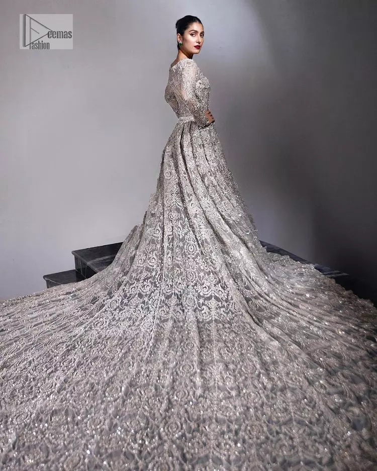 The trend of the back trains is still going strong as nikah wear – Here is the perfect one! This beautiful silver maxi is heavily embellished with silver embroidery. The gorgeous work of pearls, dabka, kora, Kundan and silver stones enhance the overall glamour of this maxi. The extraordinary design of the jewel neckline is completely embellished with silver stones and pearls embroidery combinations. The silver stones touch-up increases the looks of the beautiful gown with long tails that gives everlasting impact and at the bottom is the double flare. The full sleeves of the maxi are the lavishing style that any bride can wear on her big day.
