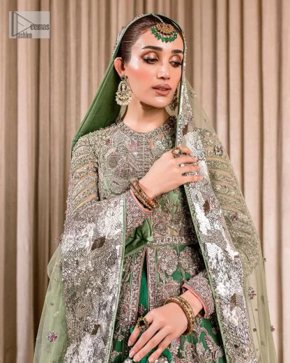 Dive into the world of ultimate allurement with this exquisitely embellished Mehndi outfit that depicts intricate glam with an elegant statement detailing. The maxi in teal green colour is heavily adorned with silver embroidery which involves tilla, dabka, kora, Kundan and the real magic of Zardozi. Further, the high neckline and full sleeves add extra glamour to this outfit. It is organized with magnificent lehenga in the same colour emblazoned with intricate gleaming embroidery which enhances the charm of this Dress. The tiny floral motifs also spread on the lehenga. Complete this article with a dupatta framed with four-sided borders and tiny floral motifs all over to make your day charming.