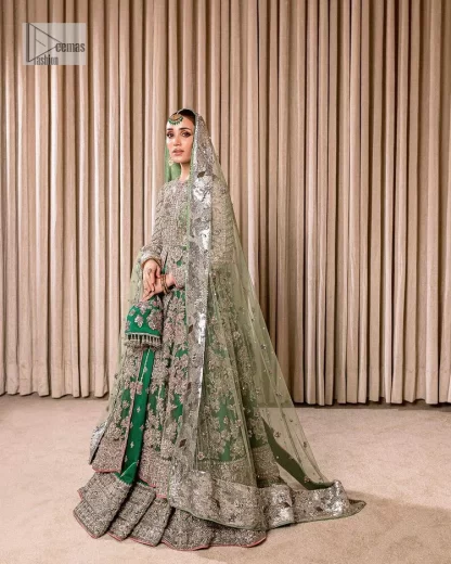 Dive into the world of ultimate allurement with this exquisitely embellished Mehndi outfit that depicts intricate glam with an elegant statement detailing. The maxi in teal green colour is heavily adorned with silver embroidery which involves tilla, dabka, kora, Kundan and the real magic of Zardozi. Further, the high neckline and full sleeves add extra glamour to this outfit. It is organized with magnificent lehenga in the same colour emblazoned with intricate gleaming embroidery which enhances the charm of this Dress. The tiny floral motifs also spread on the lehenga. Complete this article with a dupatta framed with four-sided borders and tiny floral motifs all over to make your day charming.