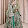 Dive into the world of ultimate allurement with this exquisitely embellished Mehndi outfit that depicts intricate glam with an elegant statement detailing. The maxi in teal green colour is heavily adorned with silver embroidery which involves tilla, dabka, kora, Kundan and the real magic of Zardozi. Further, the high neckline and full sleeves add extra glamour to this outfit. It is organized with magnificent lehenga in the same colour emblazoned with intricate gleaming embroidery which enhances the charm of this Dress. The tiny floral motifs also spread on the lehenga. Complete this article with a dupatta framed with four-sided borders and tiny floral motifs all over to make your day charming.