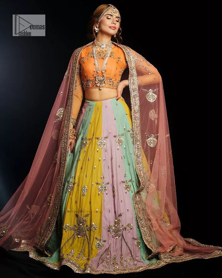 Fun colours, fresh you.  This breathtaking blouse in light orange colour is gracefully adorned with hand-crafted embellishments and lavish golden work creating a magnificent masterpiece to give you your desired appearance. The boat shape neckline of the mehndi wear is the epitome of beauty. Further, the embellished three-quarter is adorned with lavish designs and fine details making it a perfect choice to pair with the lehenga. It is organized with lehenga having multi-colour panels to give you a fresh and rainbow look on your mehndi. The lehenga is also adorned with tilla, dabka, kora, Kundan and the real magic of Zardozi. Complete this article with a dupatta, framed with four-sided borders and floral motifs on pallu to make your day Funday.