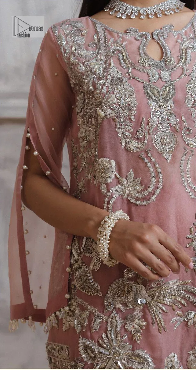 Make a style statement in this beautiful tea-pink canvas. The heavy shirt comes in a tea-pink colour and is gracefully emblazoned with silver embroidery. Hand-crafted details of sequins, tilla, dabka, kora and Zardozi give a glamorous touch to this beautiful party wear. Further, the crystalline hanging also makes this masterpiece unique and gives you a royal look. The round neckline also adds beauty to the outfit. It is paired up with trousers to balance the overall outfit.