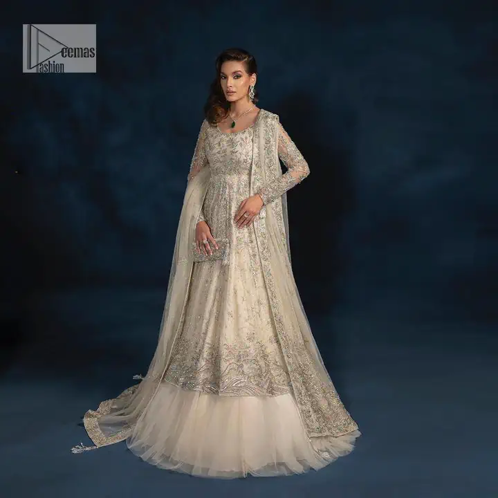 A sophisticated splash of off-white as your nikah outfit! With its round neckline and full sleeves, this outfit has a fine fusion look. Utilizing attractive silver embellishment work to enhance its intricate beauty. Tilla, dabka, kora, Kundan and the details of Zardozi beautifully embellish the elegant frock. It is paired with a flared lehenga to balance the overall look of this charming article. Finish this soft and bold look with a heavily bordered four-sided dupatta with a spray of sequins all over to make your Big day super aesthetic.
