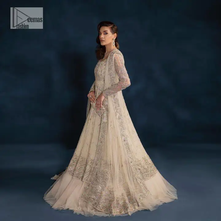 A sophisticated splash of off-white as your nikah outfit! With its round neckline and full sleeves, this outfit has a fine fusion look. Utilizing attractive silver embellishment work to enhance its intricate beauty. Tilla, dabka, kora, Kundan and the details of Zardozi beautifully embellish the elegant frock. It is paired with a flared lehenga to balance the overall look of this charming article. Finish this soft and bold look with a heavily bordered four-sided dupatta with a spray of sequins all over to make your Big day super aesthetic.